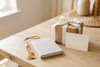 Kraft gift box with cream ribbon, blank note card, notebook, and graduation tassel on a neutral tabletop.